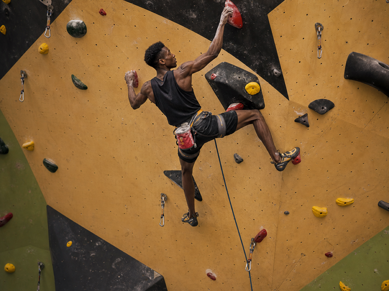 A Black lead climber high on an indoor climbing wall
